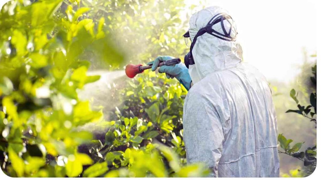 a person in protective gear spraying plants with a sprayer